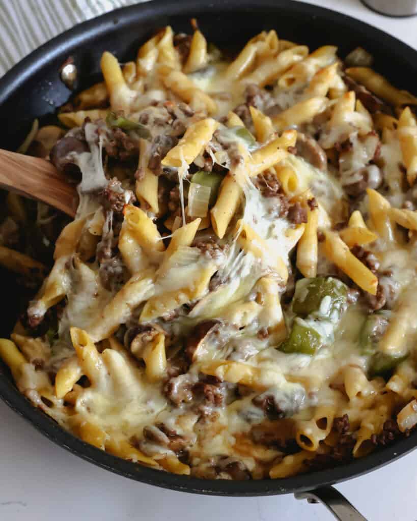 A skillet and wooden spatula full of philly cheesesteak pasta. 