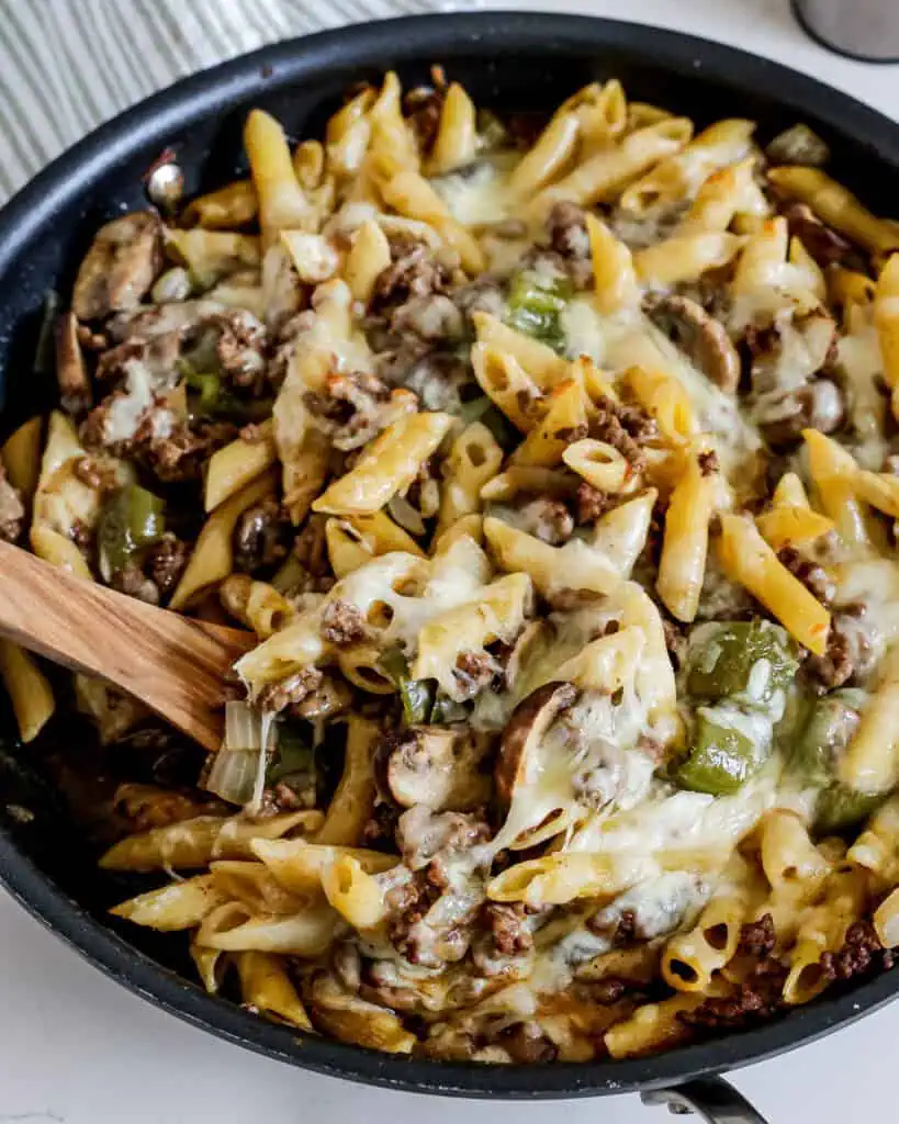 A large skillet full of Philly Cheesesteak with onions, green bell peppers, and mushrooms. 