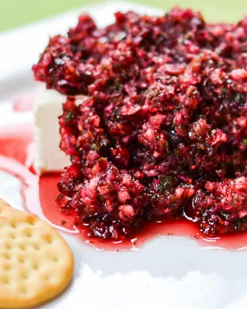 A close up view of cranberry salsa over cream cheese with Ritz crackers on the side. 