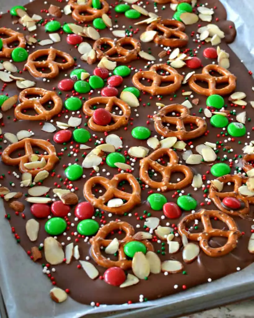 Chocolate Christmas bark with pretzels, almonds, and M&Ms on a baking sheet covered with parchment paper. 