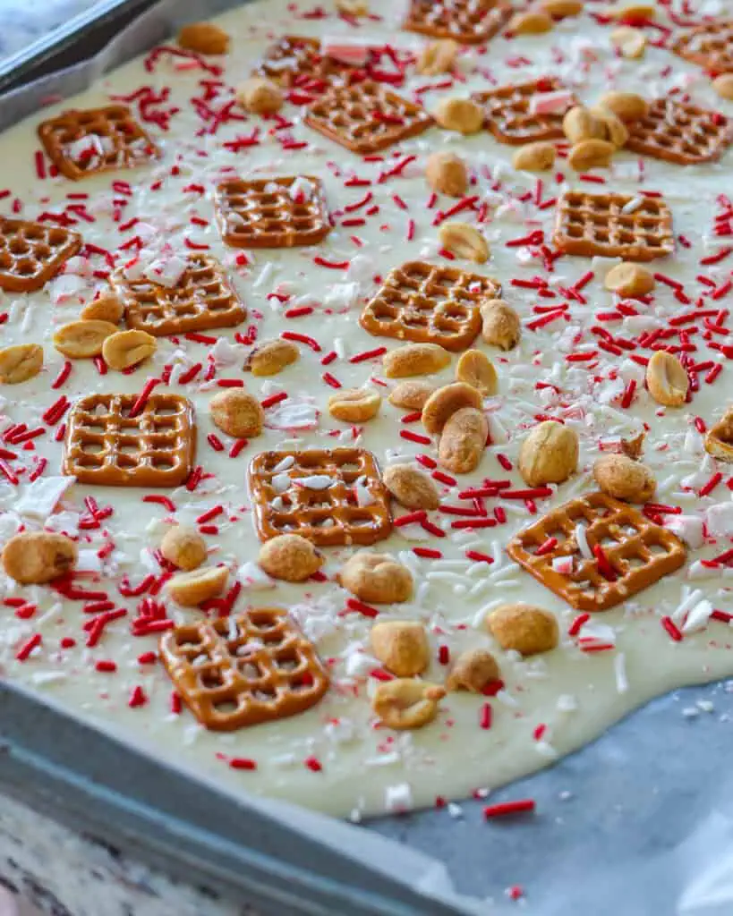 White chocolate Christmas bark with pretzels, peanuts, peppermints, and sprinkles on a king sheet covered with parchment paper.  