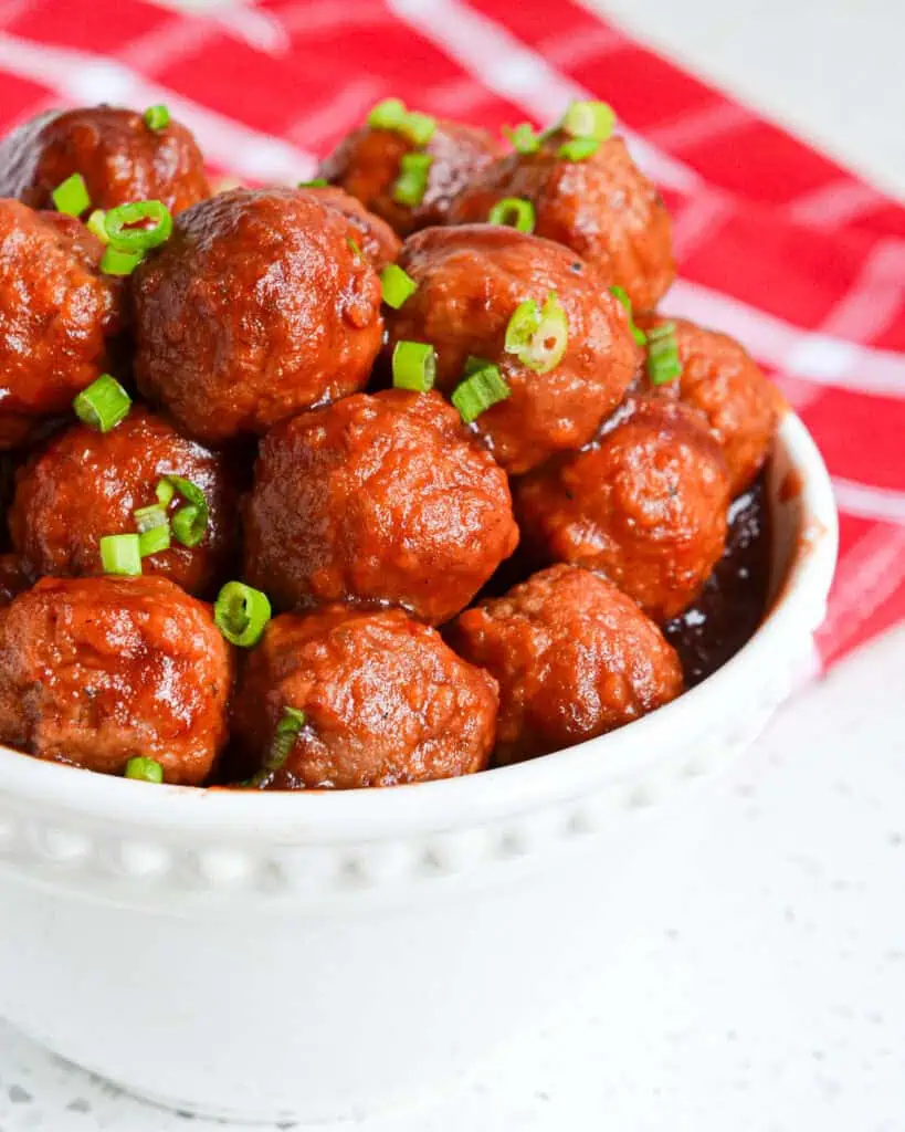 Cranberry meatballs topped with green onions in a bowl. 