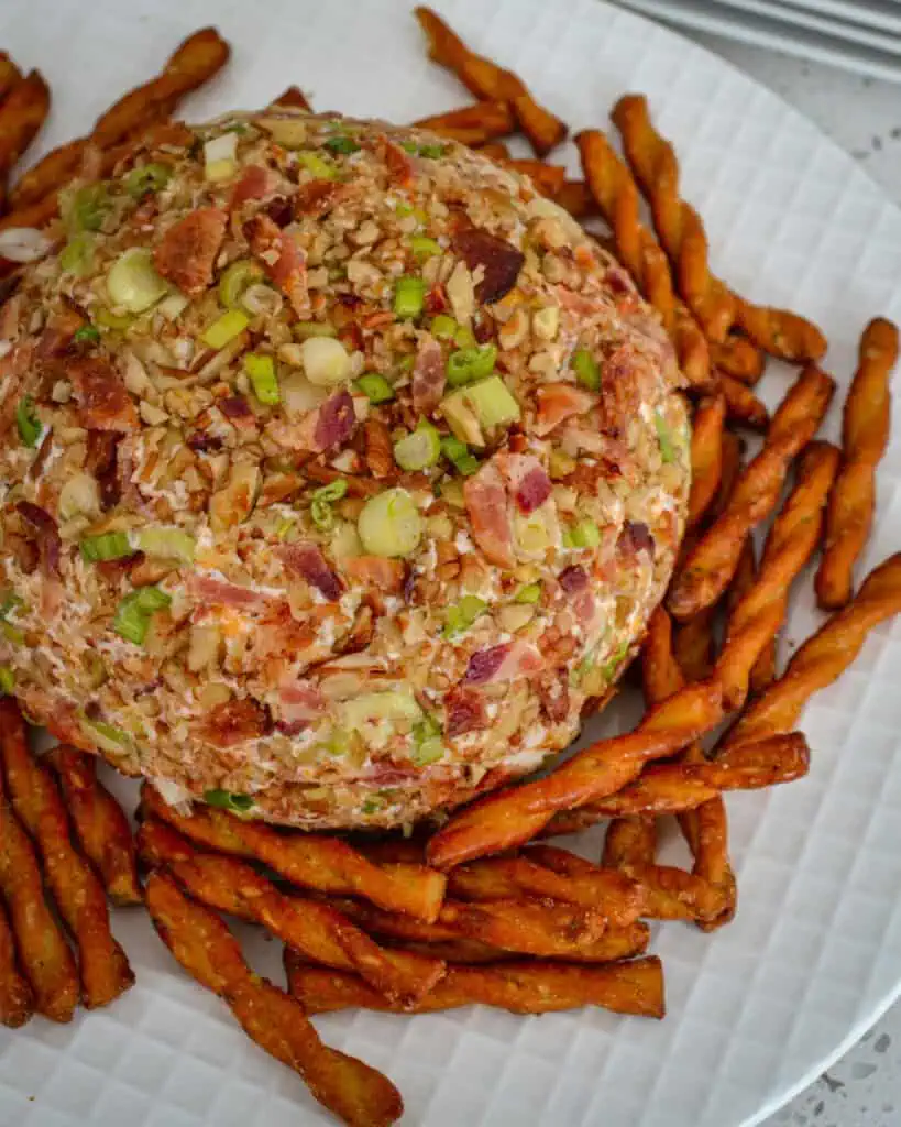 An overhead view of a bacon ranch cheese ball on a plate with pretzel twists. 