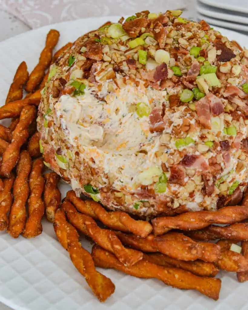 A bacon ranch cheese ball on serving  plate with pretzel twists. 