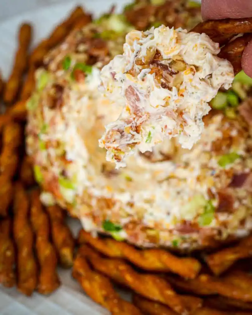 A close up view of a part of a bacon ranch cheese ball on pretzel twists. 