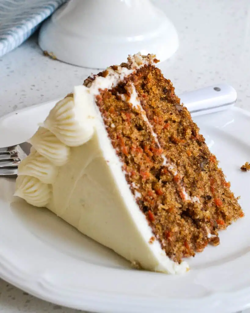 A slice of carrot cake with cream cheese frosting on a single serving plate. 