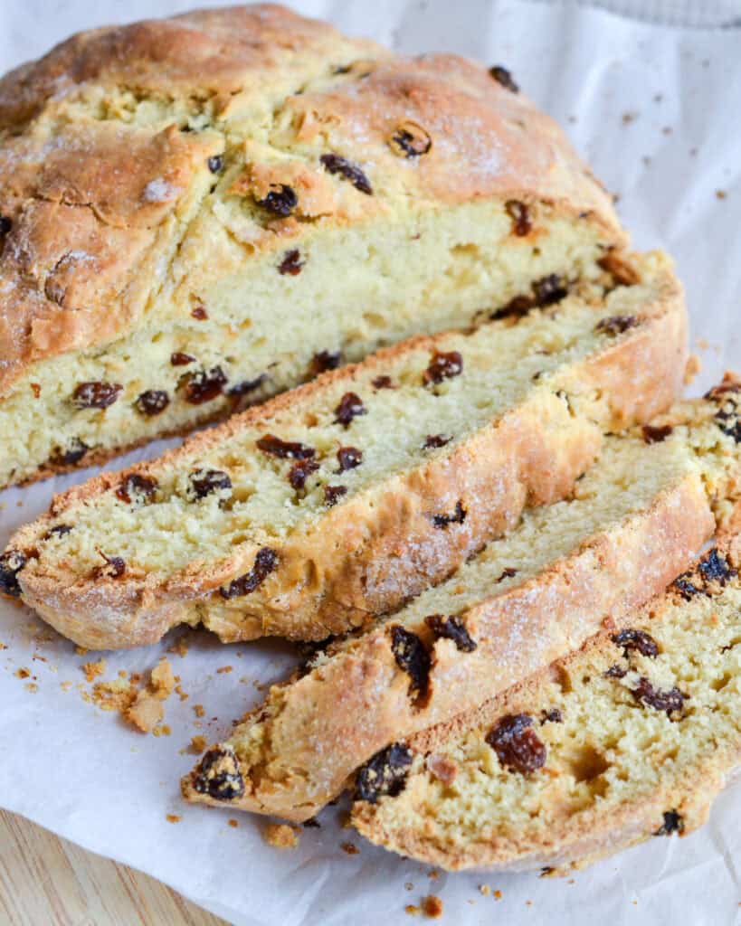 A sliced loaf of Irish soda bread with raisins on parchment paper. 