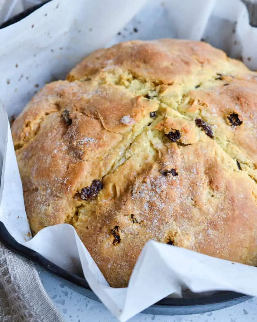 A whole classic Irish soda bread in parwchment paper on a baking sheet. 