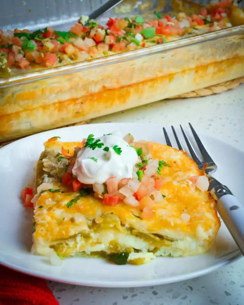 A slice of chile relleno casserole on a plate in front of the rast of the casserole dish. 