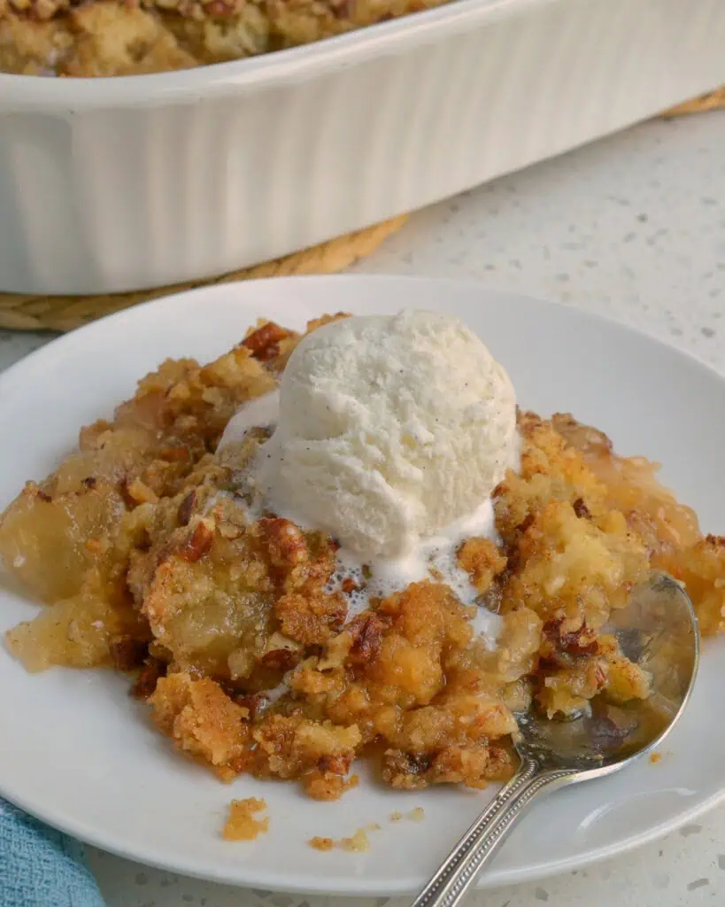 Apple dump cake wth a scoop of vanilla ice cream and a spoon. 