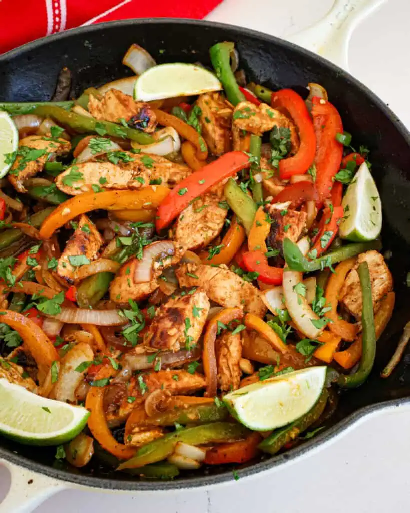 A close up view of chicken fajitas with chopped cilantro and lime wedges. 