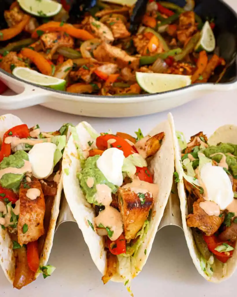 Chicken Fajitas with lettuce, sour cream, guacamole, and chopped cilantro in front of a skillet full of chicken fajitas, 