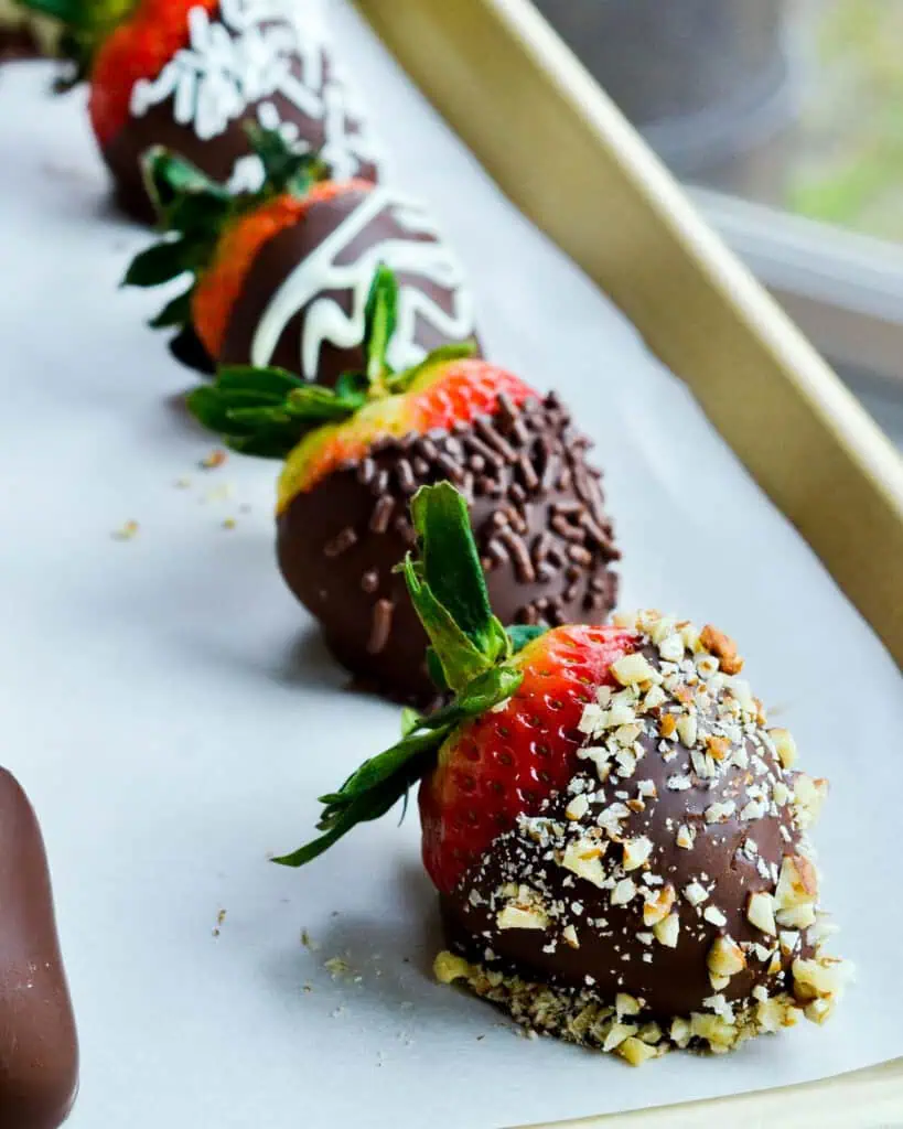 A close up view of chocolate covered strawberries on a parchment covered baking sheet. 