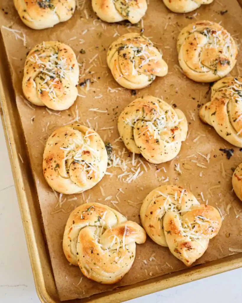 Fresh baked garlic knots on a baking sheet covered with parchment paper. 