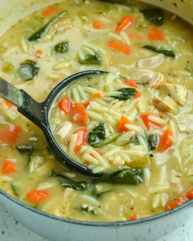 A quick and simple creamy chicken orzo soup with a touch of lemon in a Dutch oven with a ladle. 