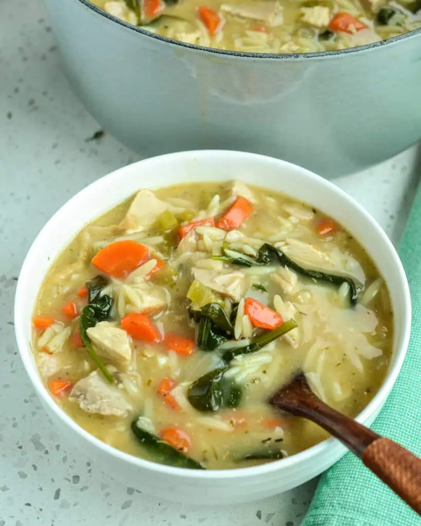 A bowl full lemon chicken orzo soup with a wooden spoon in it. 