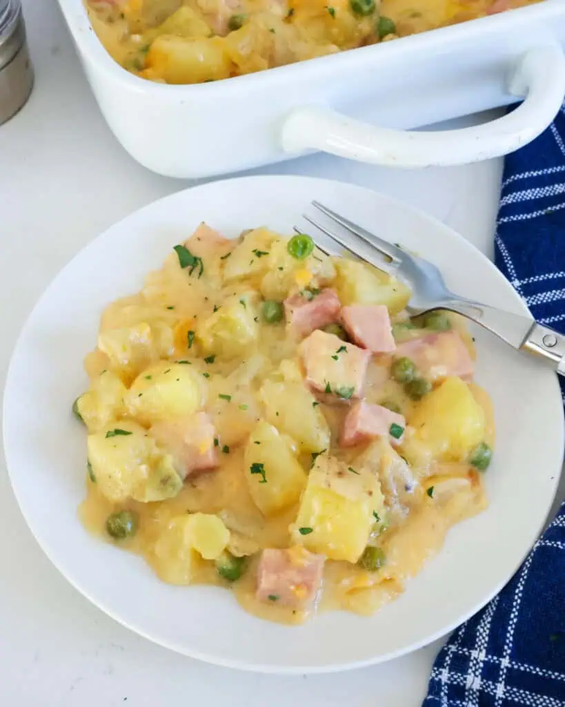 Cheesy ham and potato casserole on a single serving plate with a fork on the side. 