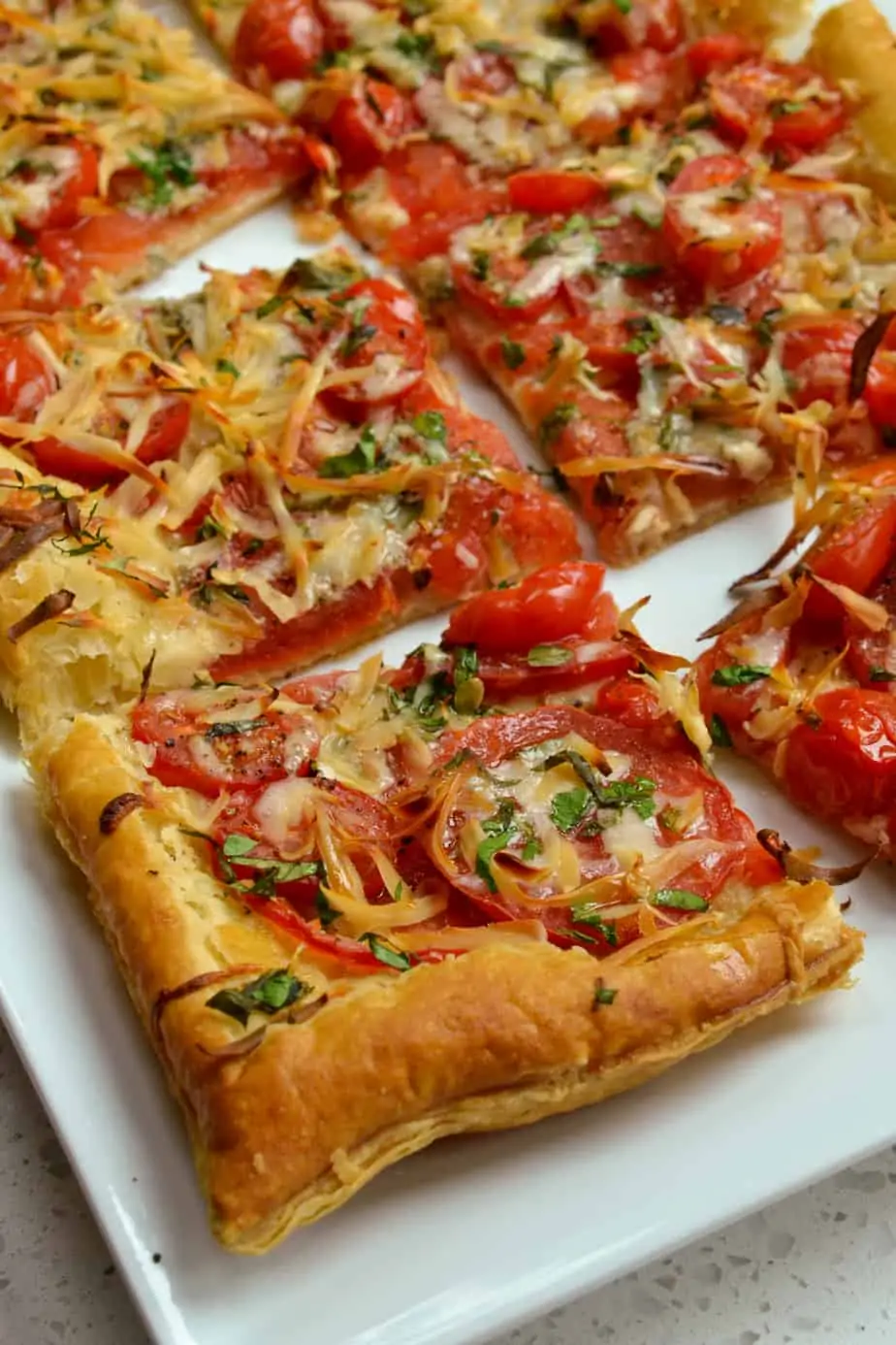 Tomato Tart is made easily with frozen puff pastry, garden fresh tomatoes, fresh herbs, mozzarella, cheddar, and gruyere cheese. 
