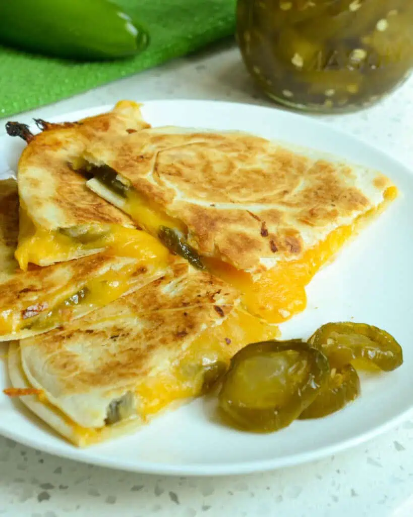 A cheese and candied jalapeno quesadilla. on a single serving plate with more candied jalapenos. 