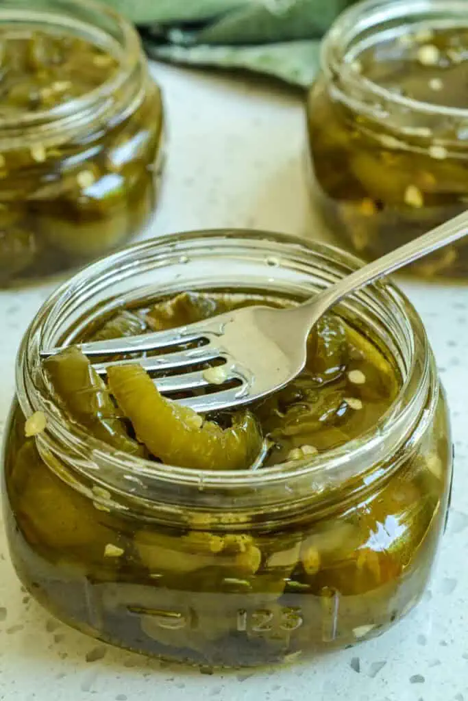 A small jar of candied jalapenos with a fork in it. 