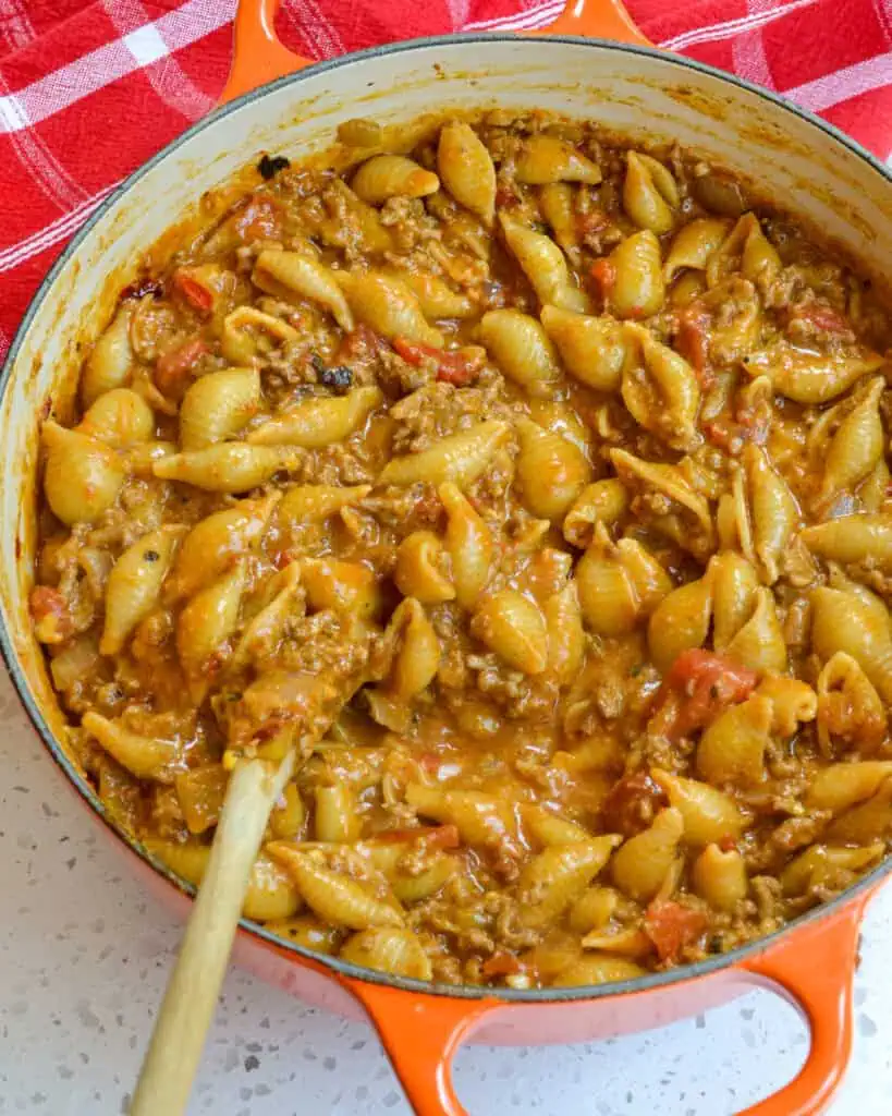 A Dutch oven and woooden spoon full of cheesy taco pasta. 