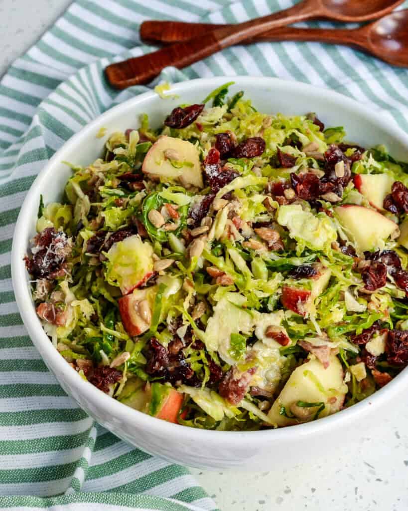 Brussels sprouts in a bowl with a kitchen towel and serving spoons in the background. 
