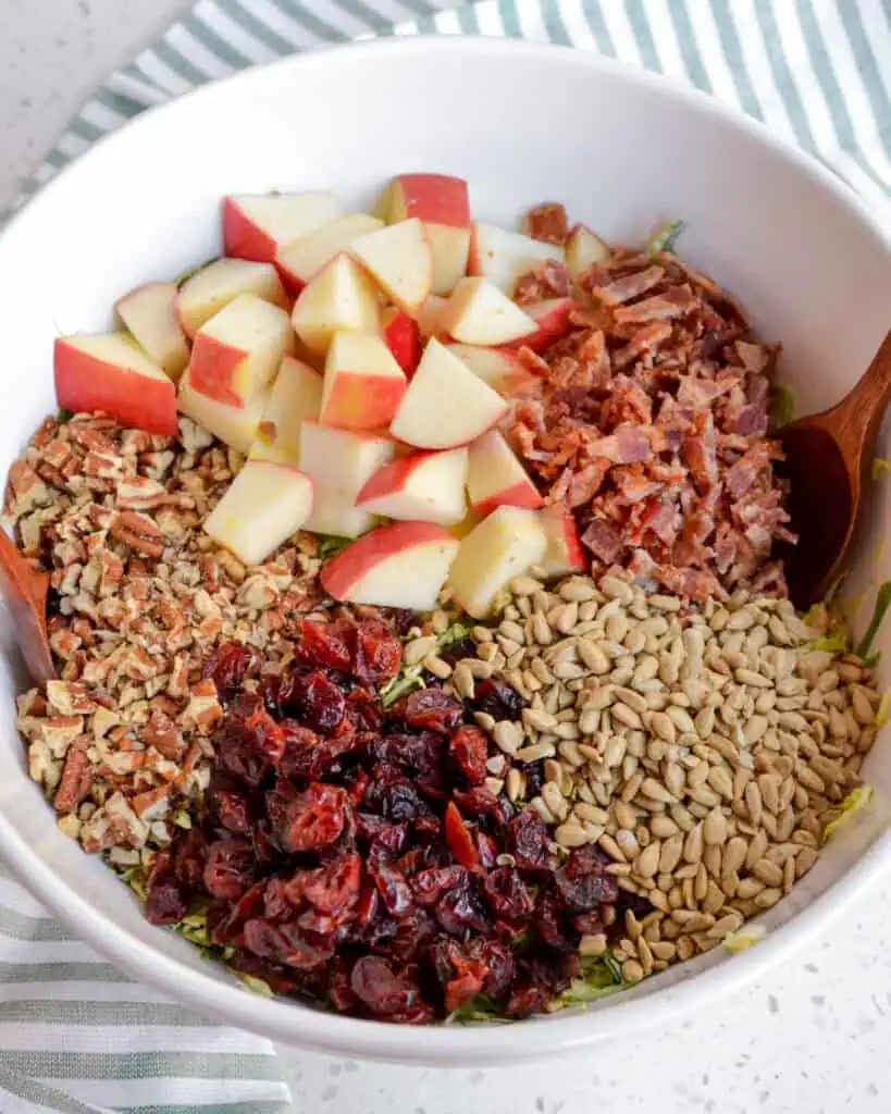 Combine the shaved Brussels sprouts, apples, pecans, cranberries, bacon, sunflower seeds, and Parmesan cheese in a large bowl.