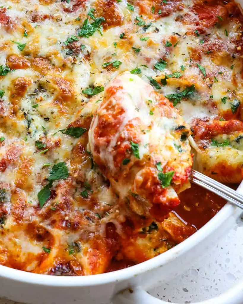 A metal spoon holding a ricotta and spinach stuffed pasta shell.