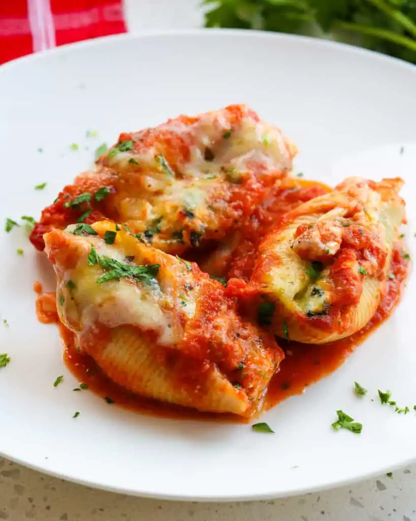 Three baked stuffed shells on a single serving plate . 