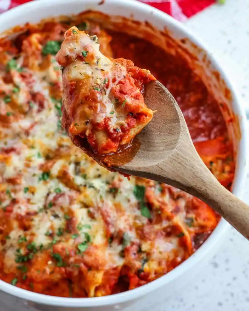 A wooden spoon with a ricotta stuffed shell over a casserole full of ricotta stuffed shells. 