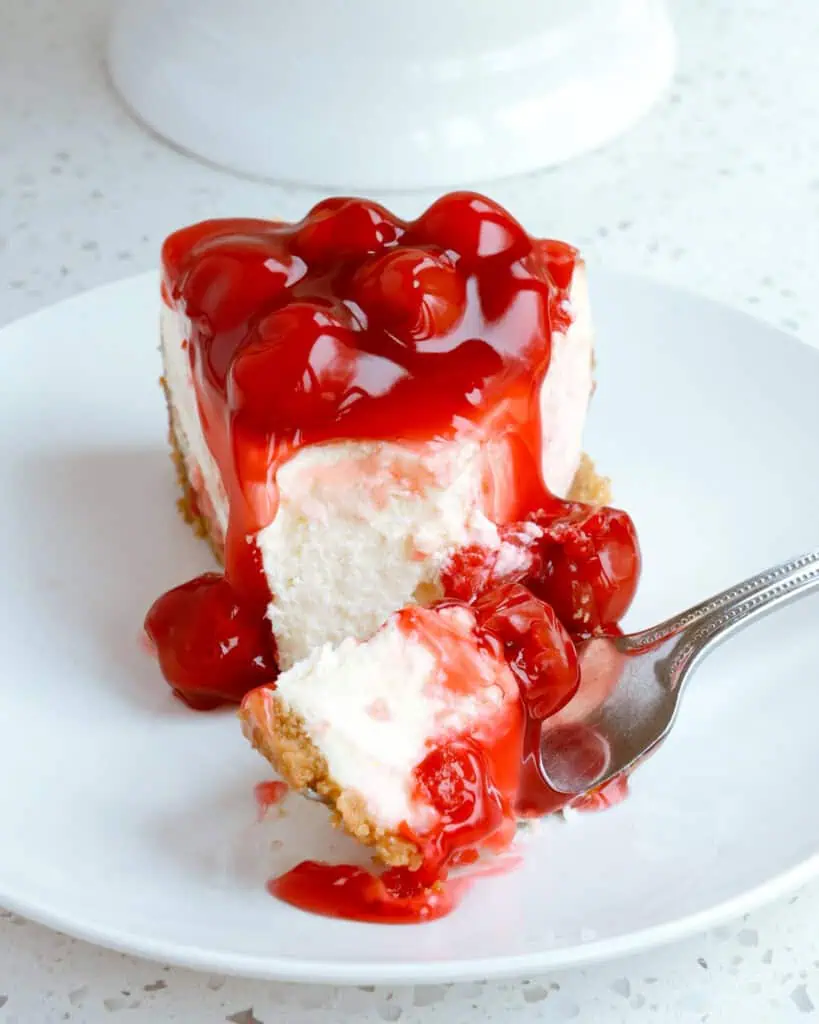 A single slice of cheesecake with cherry topping on a plate with a fork. 