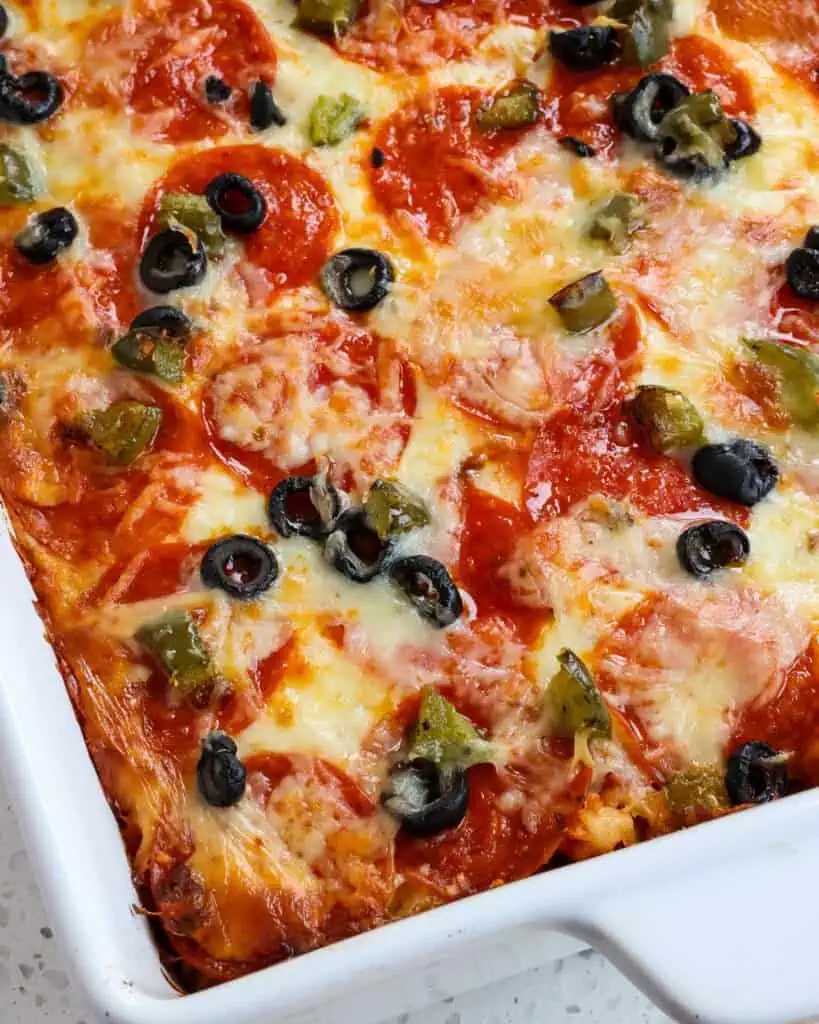 A close up view of pizza casserole with pepperoni, black olives  and green pepper. 
