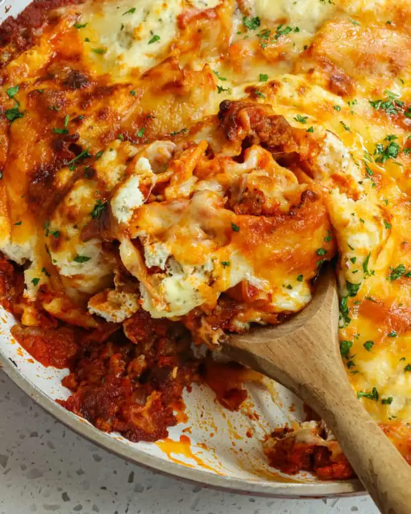 A large skillet and a wooden spoon full of skillet lasagna. 