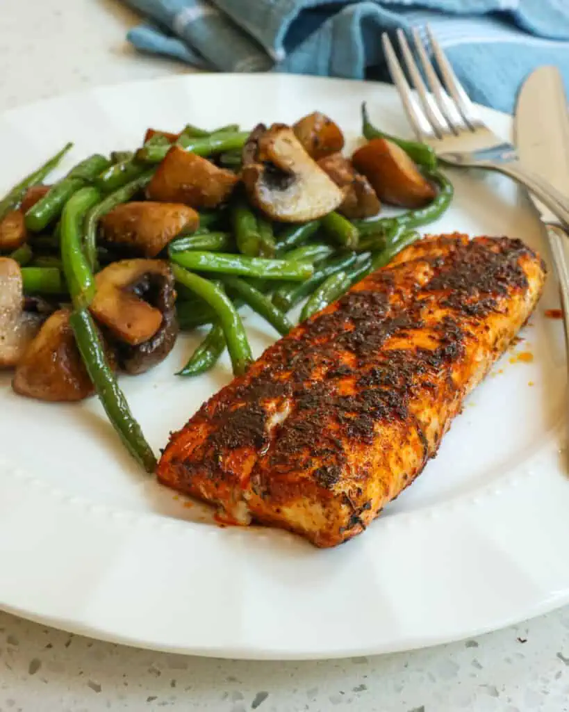 Blackened Mahi Mahi on a serving plate with green beans and mushrooms and a fork and a knife on the plate. 