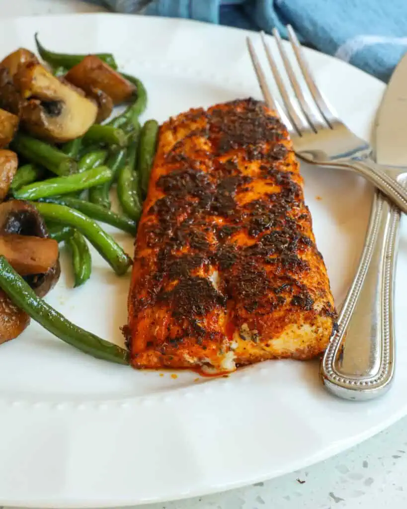 A filet of blackened Mahi Mahi with green beans and mushrooms on a serving plate. 