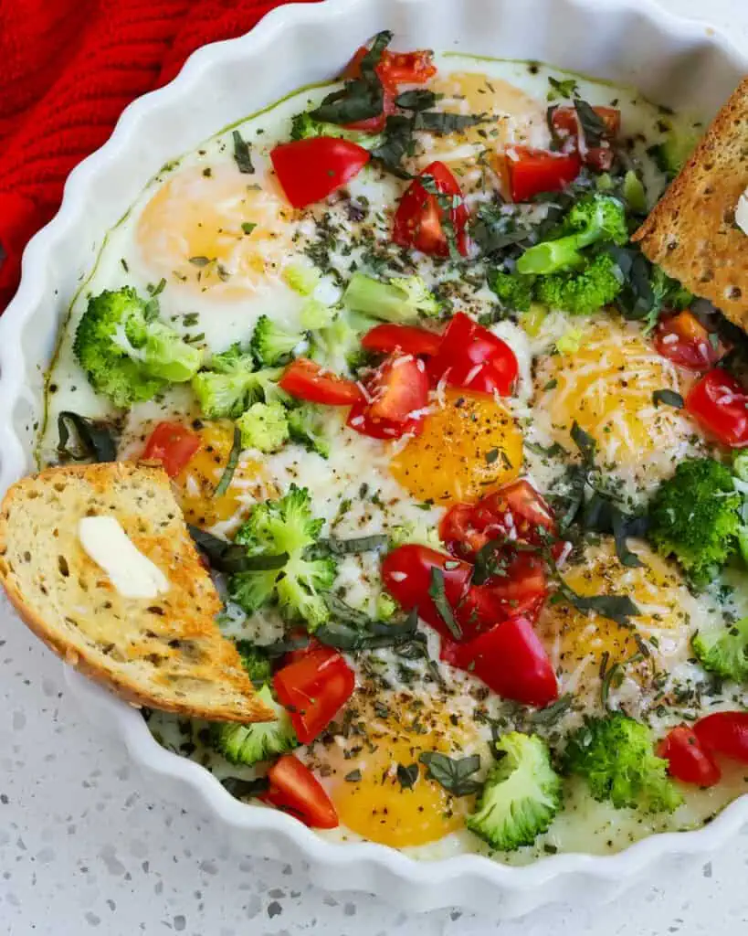 Baked eggs with broccoli, tomatoes, and fresh herbs with a side of toast. 