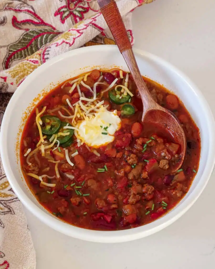 Instant pot chili in a bowl with sour cream, cheese, and jalapeno rings. 