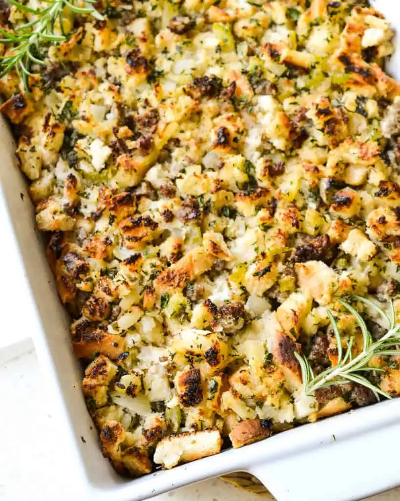 A casserole dish full of Thanksgiving sausage stuffing with fresh herbs. 