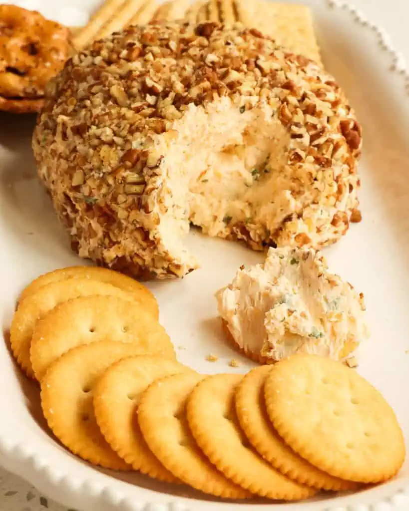 A cheese ball on a platter with a helping of the cheese ball on a cracker. 