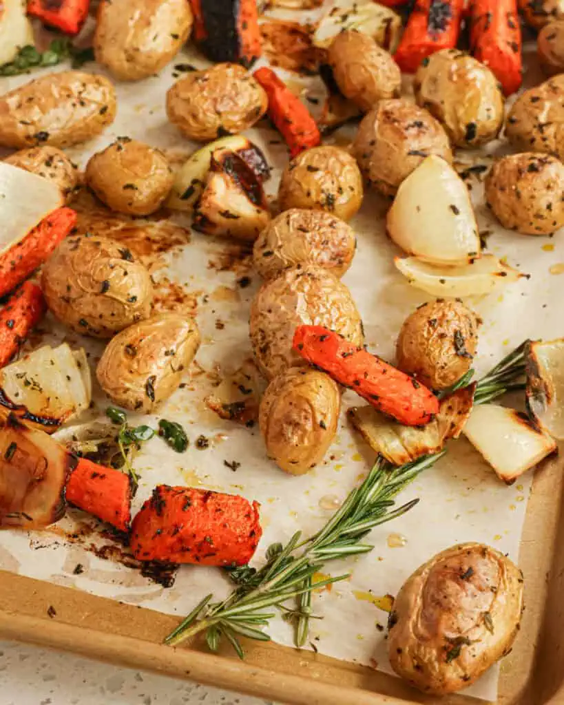 Roasted carrots, potatoes, onions, and rosemary on a baking sheet covered with parchment paper. 