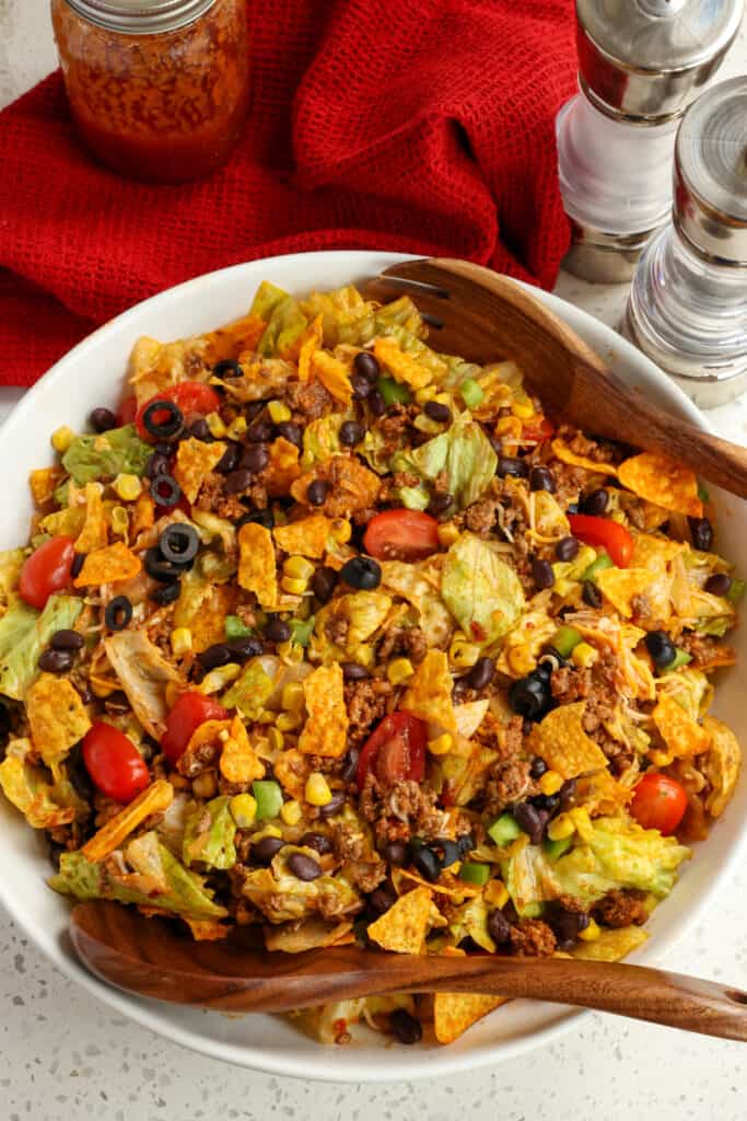 Doritos taco salad in a large bowl with two wooden serving spoons, 