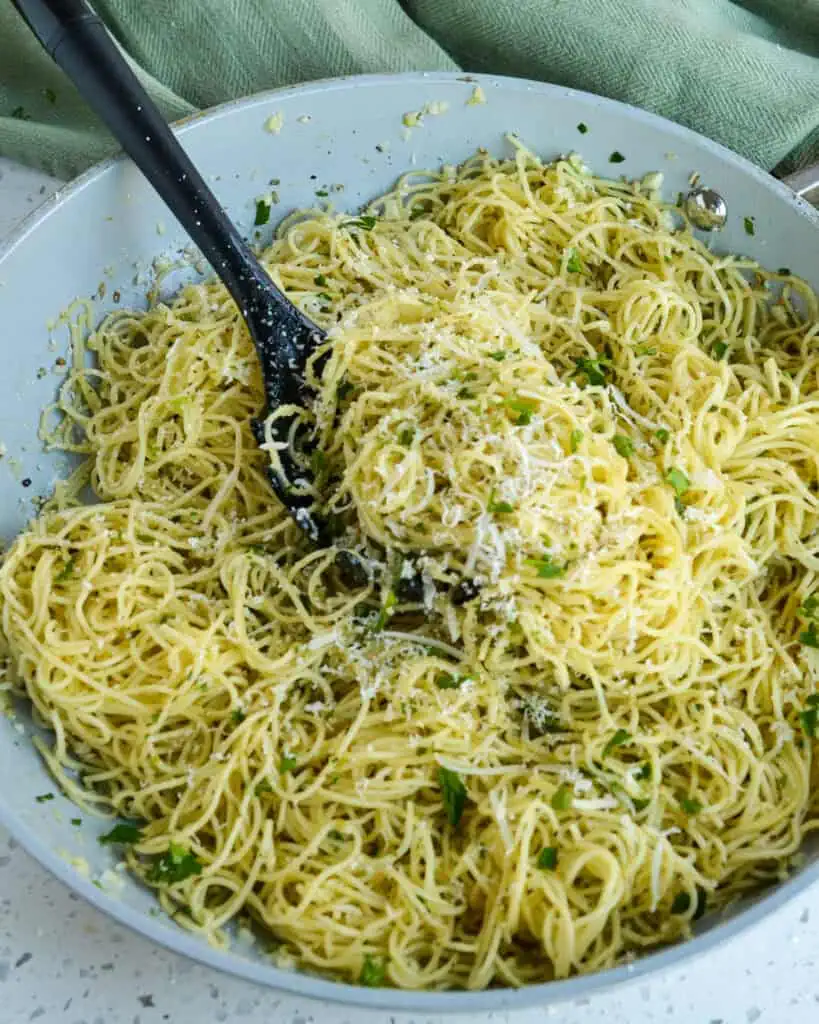 A large skillet full of angel hair pasta with grated Parmesan cheese and fresh parsley. 