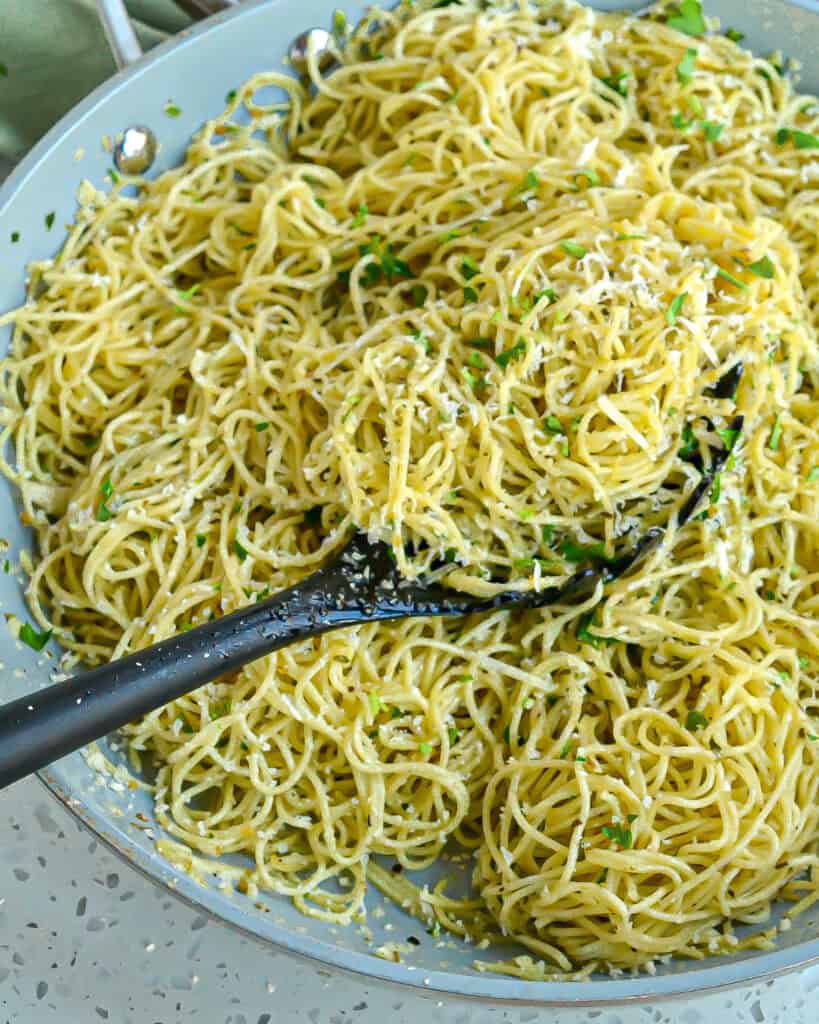 A spoon full of angel hair pasta with fresh herbs and Parmesan cheese. 