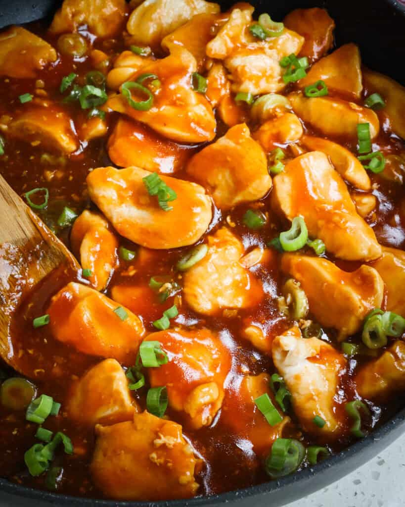 Bourbon Chicken in a skillet with a wooden spoon. 