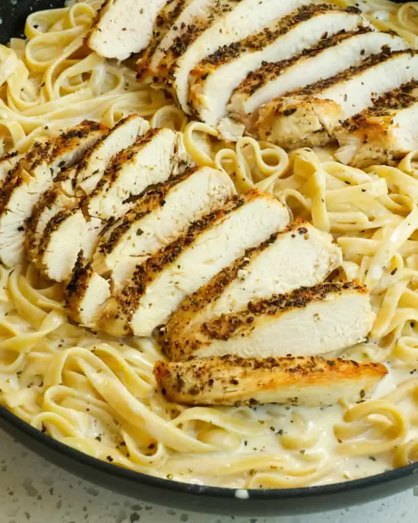 Fettuccine alfredo with sliced seasoned chicken on top. 