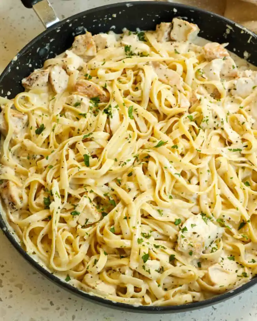 A large skillet full of chicken fettuccine alfredo with chopped fresh Italian parsley. 