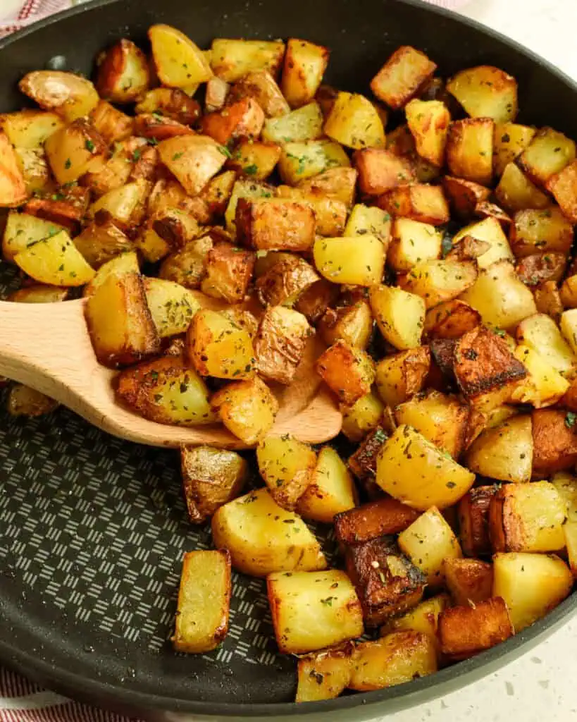 A large black skillet full of pan fried potatoes with seasoning. 