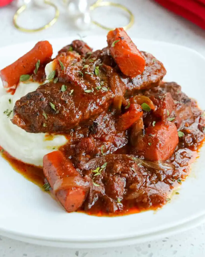 Swiss steak with carrots, onions, and garlic, over mashed potatos on a round serving plate. 