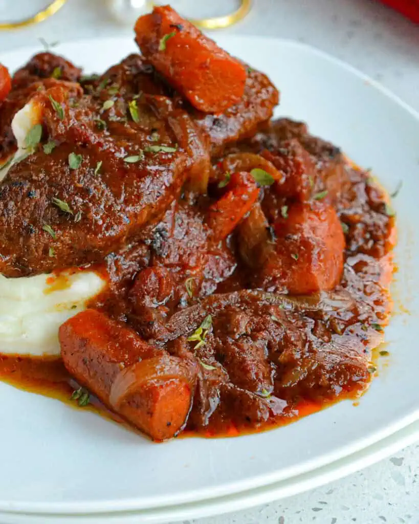 A close up view of Swiss steak with carrots, onions, and fresh herbs over mashed potatoes. 