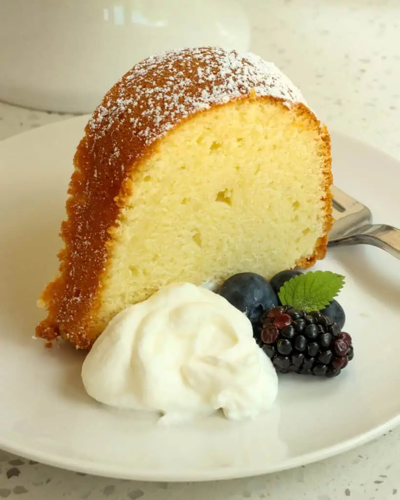 A slice of cream cheese pound cake on a plate with whipped cream, blackberries, blueberries, whipped cream, and a fork. 